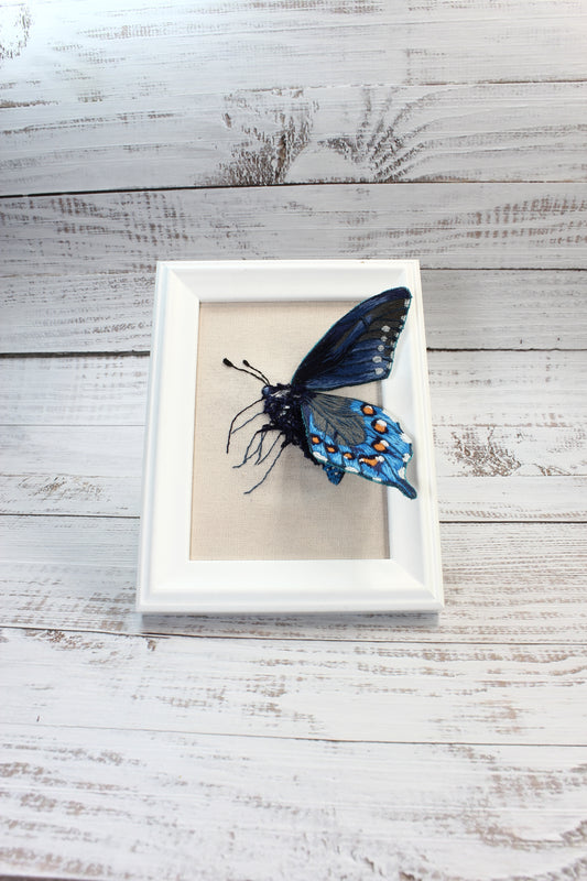 Framed artwork of a blue butterfly on a wooden surface