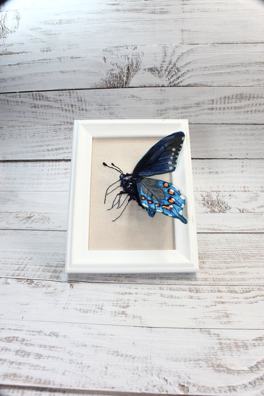 Framed artwork of an embroidered butterfly on a wooden surface