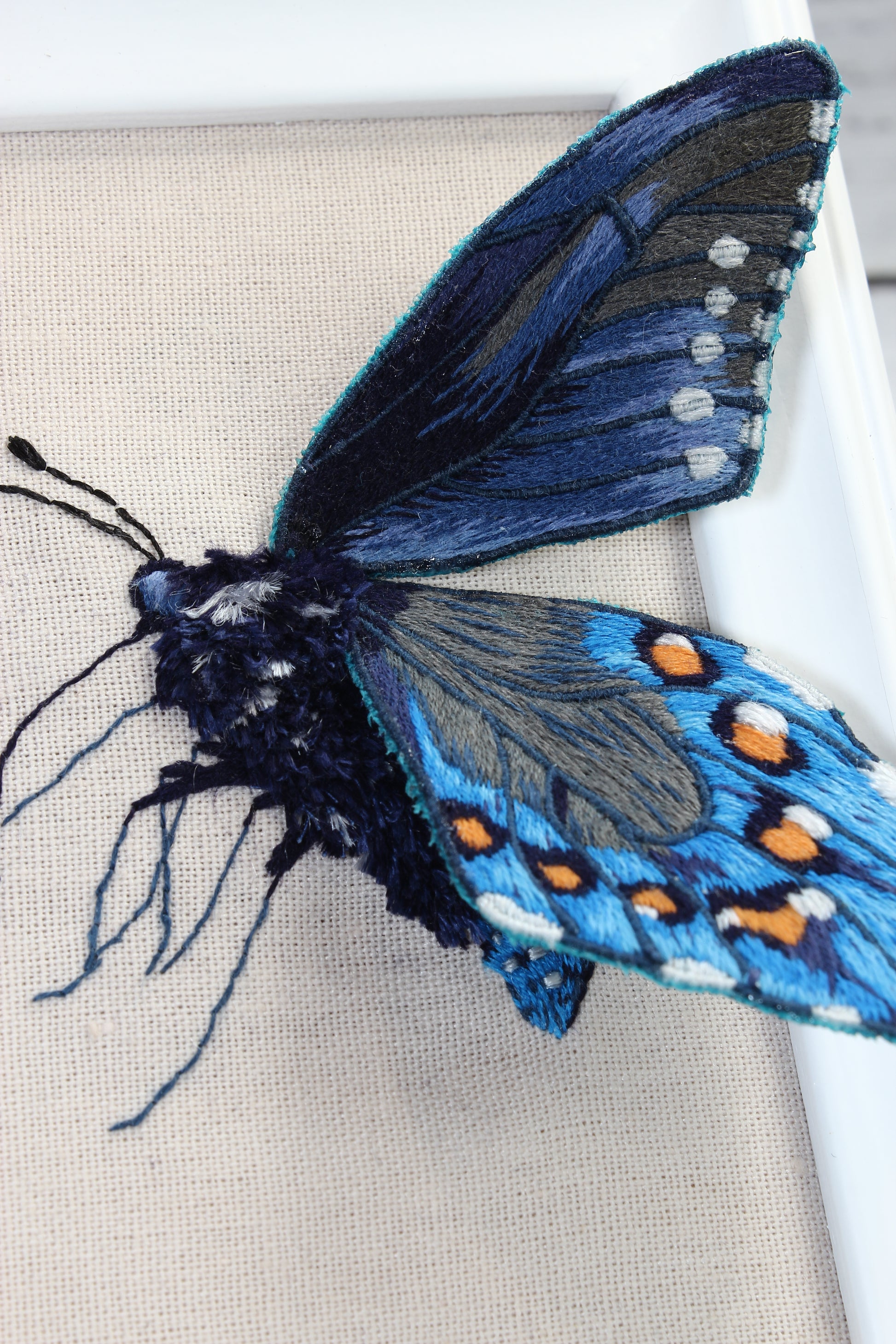 Embroidered butterfly with blue and black wings on a beige background