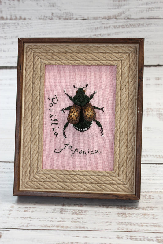 Framed artwork with a beetle embroidery and text on a pink background