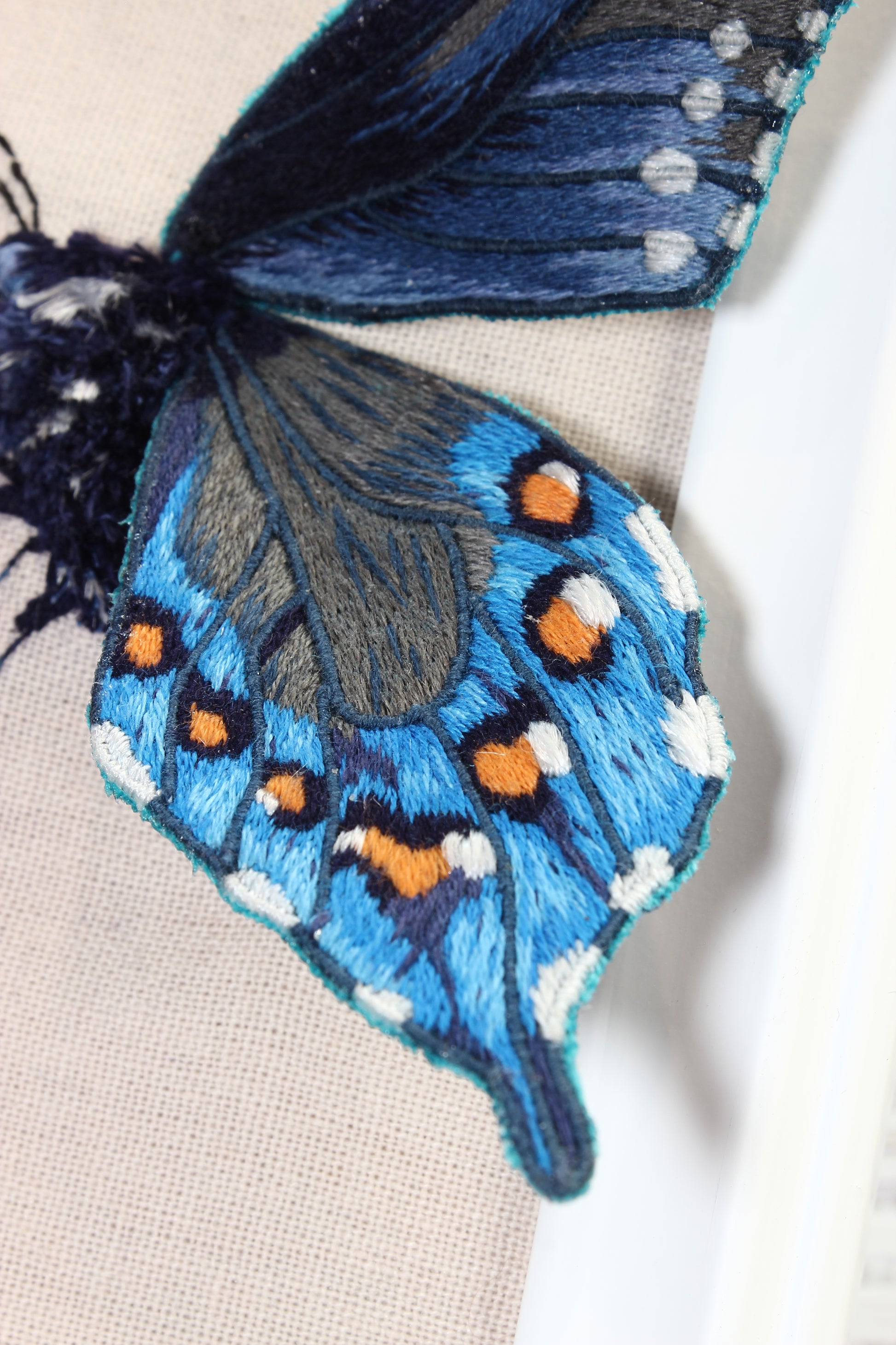 Embroidered butterfly with blue, orange, and black colors on a beige background